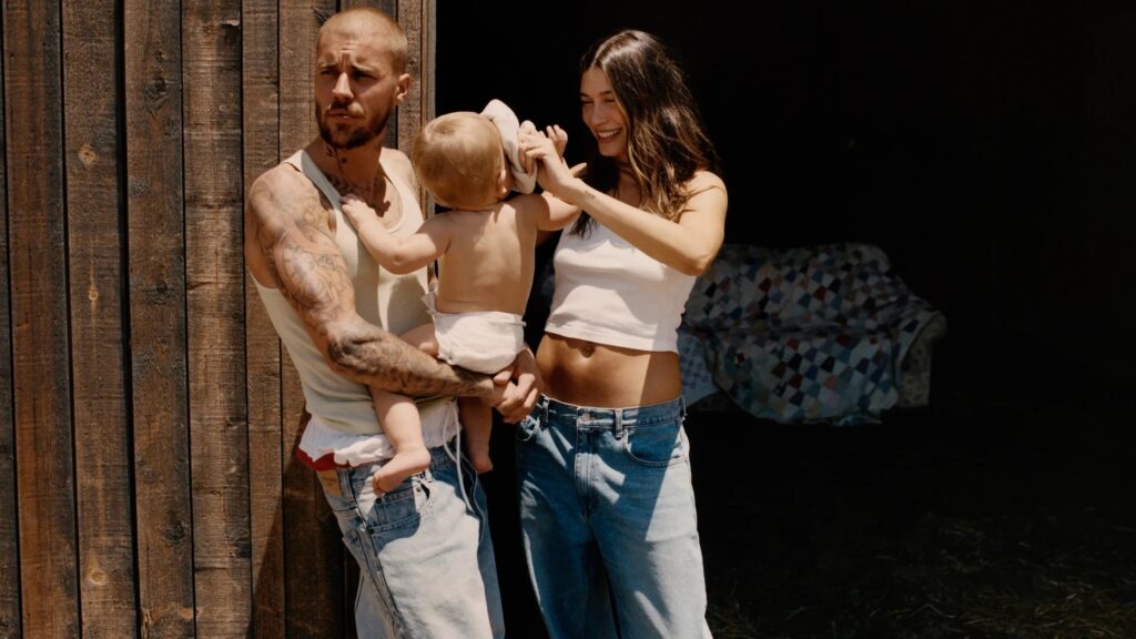 Justin Bieber carrying his son and his wife hailey bieber standing next to him rubbing their son's head