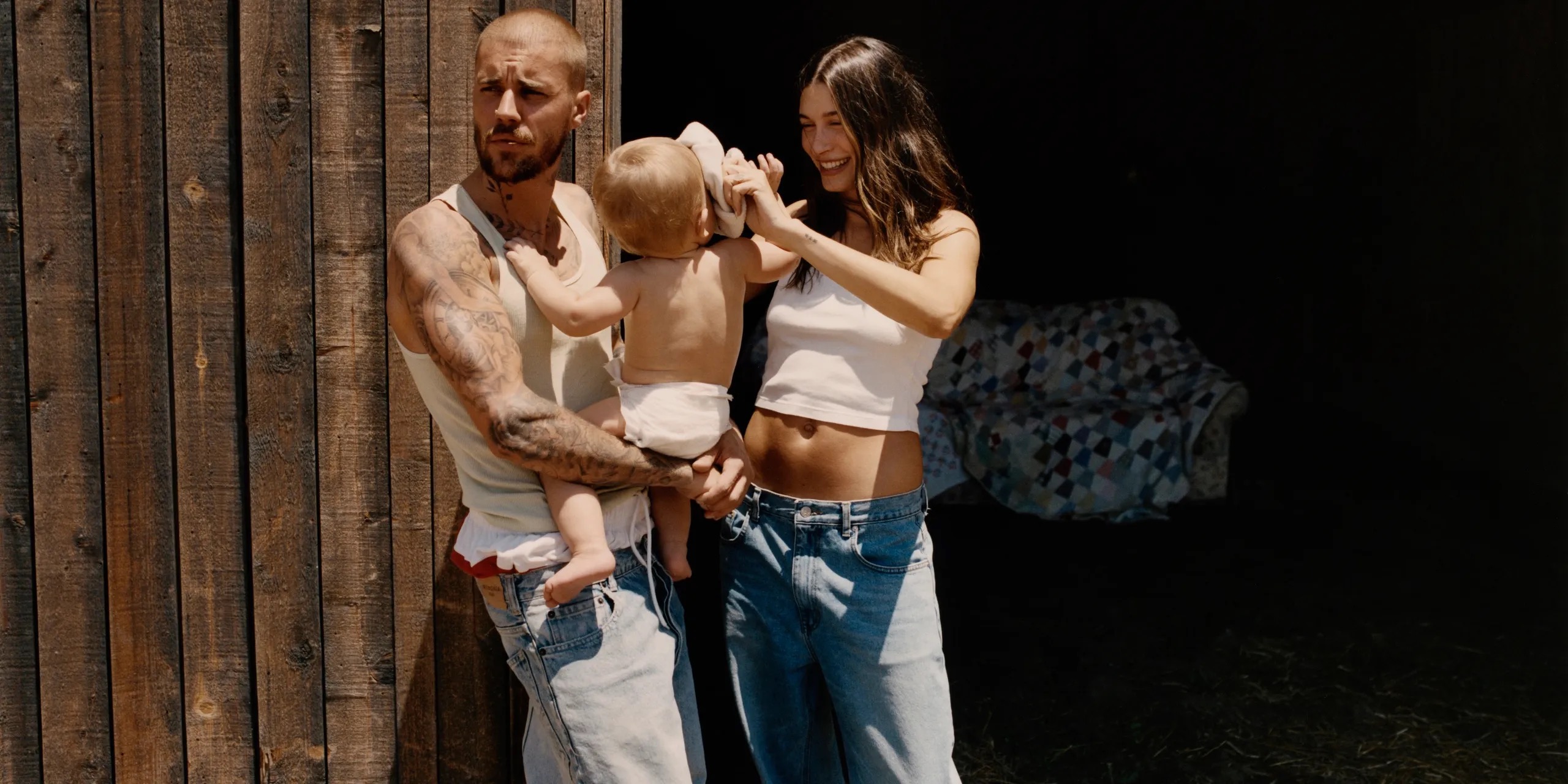 Justin Bieber carrying his son and his wife hailey bieber standing next to him rubbing their son's head